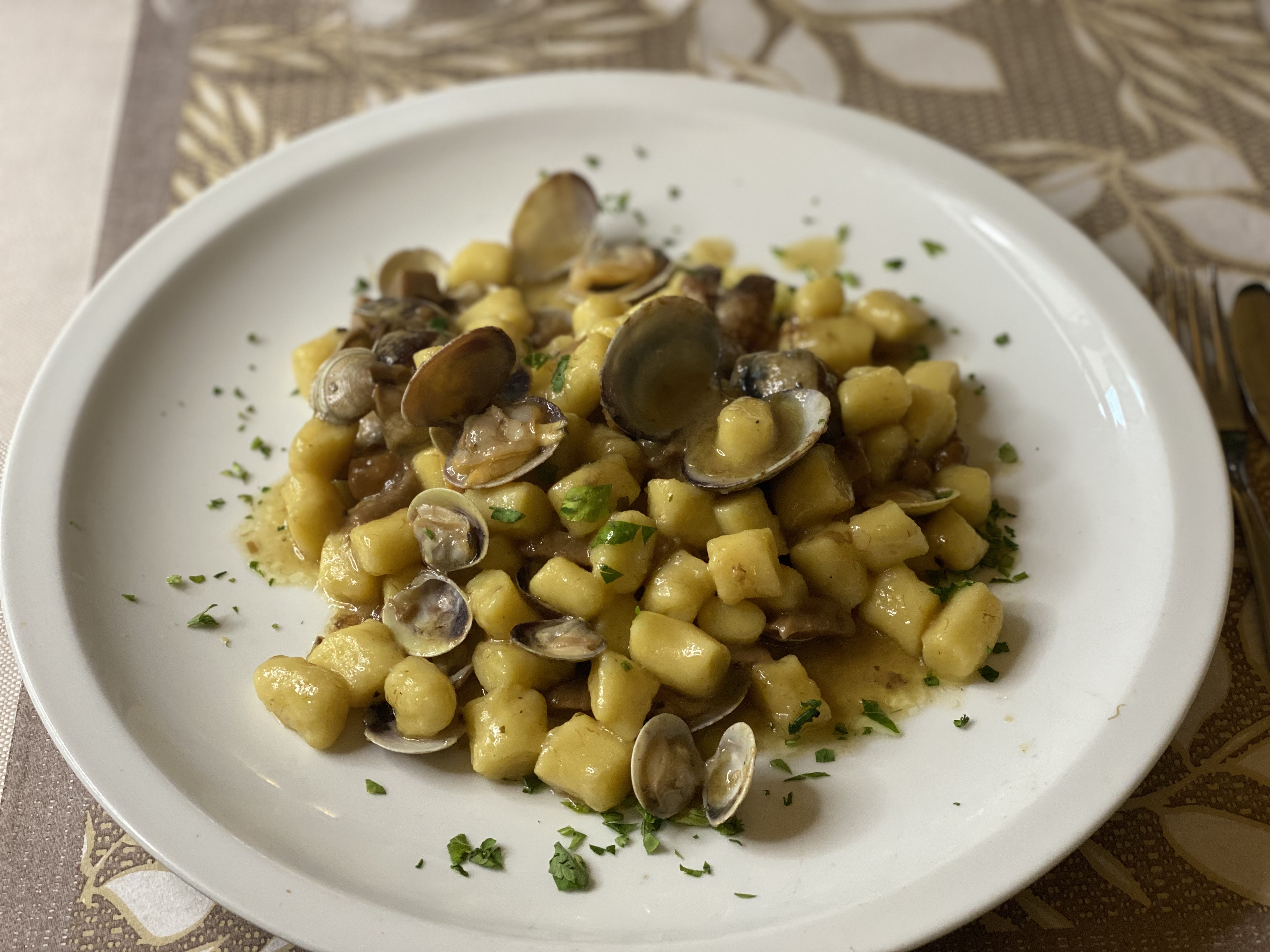 #AzaleaSalinaSpa - A close-up shot of homemade pasta with clams. The white plate displays a dish of gnocchi covered in cla...